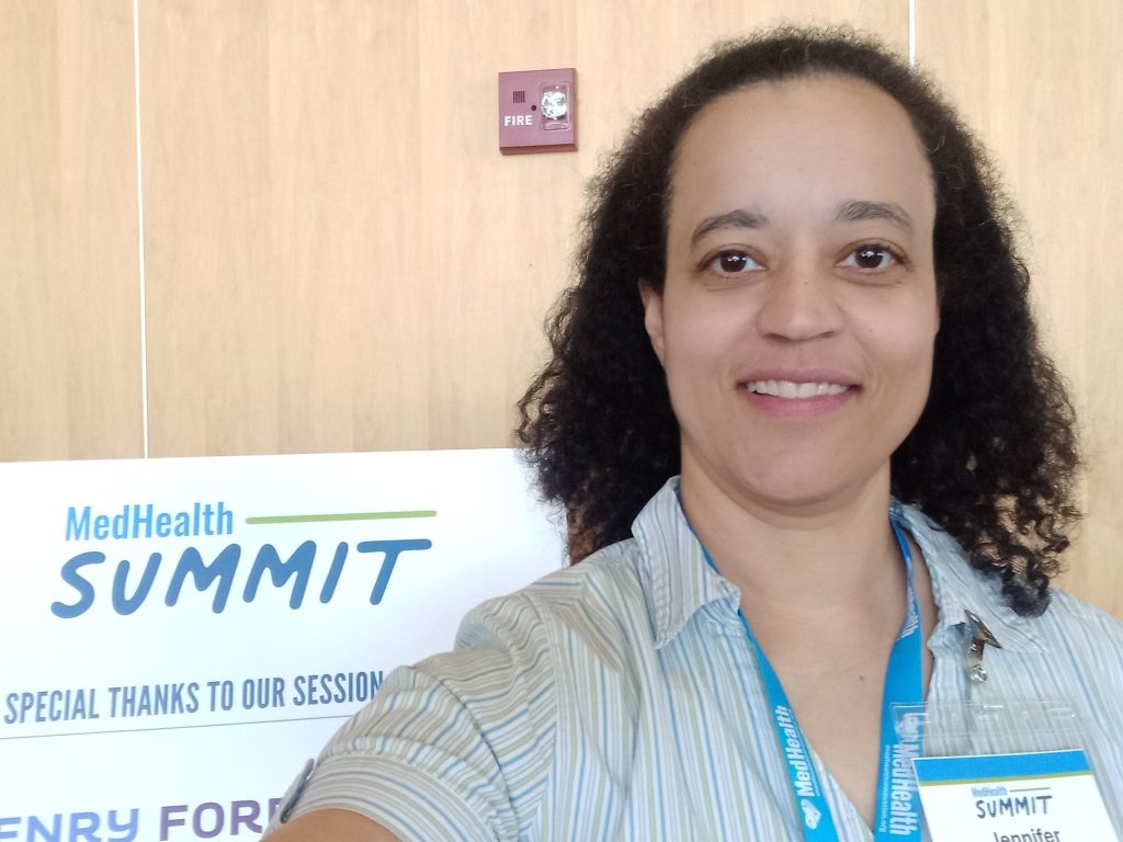 Selfie of Jennifer German standing next to sign that says "MedHealth SUMMIT"